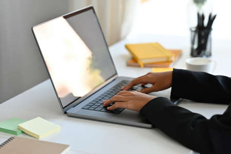 Close-up image of a businesswoman's hand typing on a white blank screen computer laptop at the...