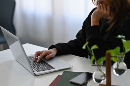 Cropped image of a woman typing on a computer laptop at the white working desk.