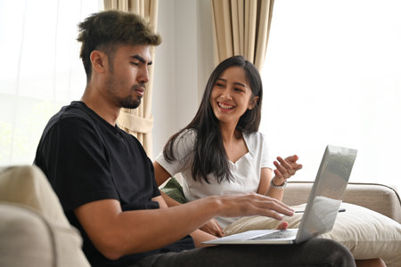 Young Asian couple  sitting on sofa together while a man looking on laptop, Domestic life and...