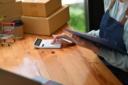 Close up with mall business owner working with calculator, The seller prepares the delivery box for the customer with postal parcel. Selling online and delivery.の写真素材