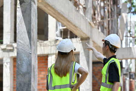 Construction engineer and architect point to the construction site. wearing safety vests and helmets...
