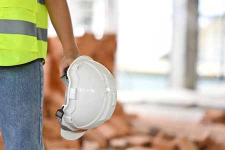 Close up with hands of an engineer holding white safety helmet with building construction site as...