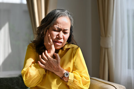 Senior female feel stressed suffering from severe toothache while sitting on sofa at home, health...