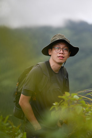 Portrait of a young Asian adventurer standing in a pose, with fog and mountains in the background.の写真素材