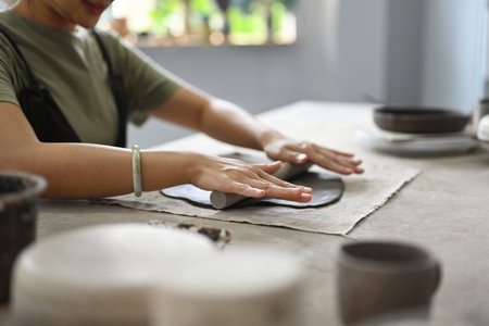 Close up and cropped image with Woman potter master rolling with pin while preparing clay mug, production process of handicrafter pottery. Ceramic making concept.の写真素材