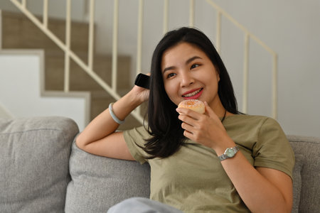 Young Asian woman enjoy with her entertainment program on TV while eating a snack.
