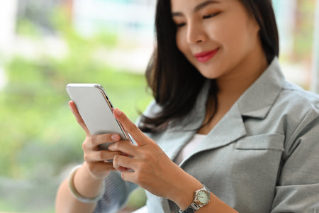 Close up and Cropped image of Happy and cheerful Asian businesswoman in formal suit using smartphone.の写真素材