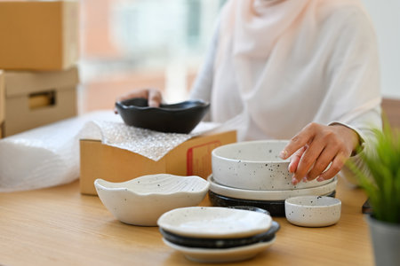 Close up and cropped with Muslim woman with headscarf packing crockery into the post box for send to...