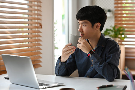 Portrait with Young Asian Businessman looking out of the window while sipping coffee in the morning.の写真素材