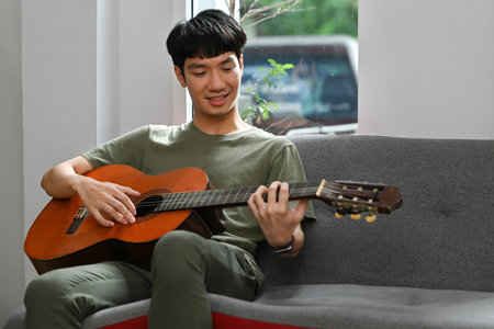 Millennial Young Asian male playing classic guitar in the living room, Hobby and lifestyle concept.