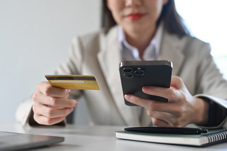 Young adult Asian female consumer holding credit card and smartphone. E-commerce, online banking transaction and shopping online.の写真素材