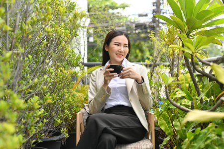 Modern asian  businesswoman with formal clothes enjoying her morning coffee, sitting outside office building.の写真素材