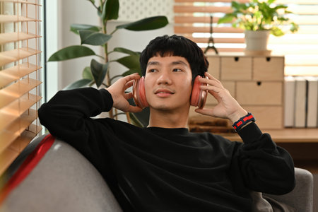 Young millennials enjoy music on headphones while sprawling on the couch.