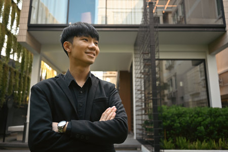 Portrait of successful real estate agent posing with arms crossed gesture against apartment on...