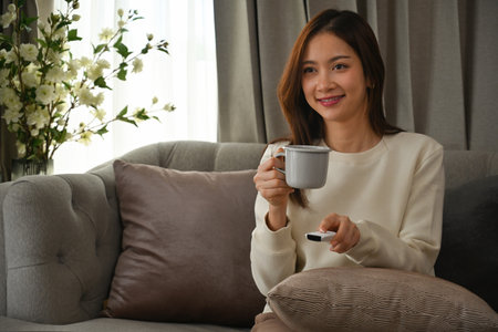 Portrait with Young Asian woman holding a remote control and enjoy with coffee at home.