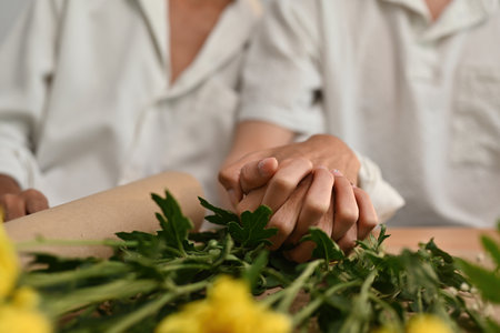 Selective focus on clasped hands together between young asian gay, home flower arrangement...