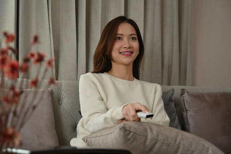 Young Asian female dazzled feeling amazed while watching television at home.の写真素材