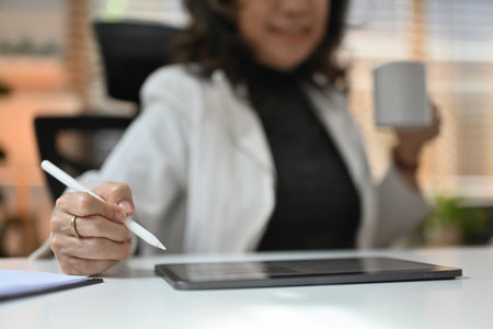 Close up with Senior Mature Asian Business woman using stylus pen and digital tablet for working while holding a cup of coffee.の写真素材