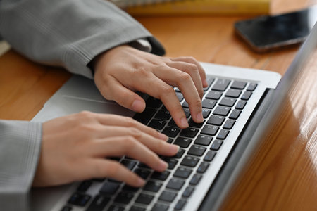 Close up and cropped image of Young businesswoman's hand with suit typing on laptop keyboard.