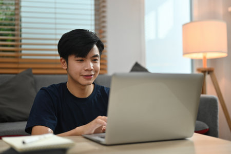 Young Asian man using laptop while sitting in the living room at home.の写真素材