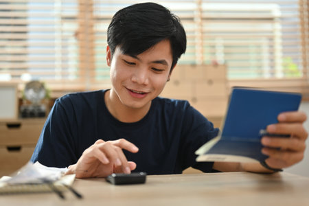 A Young Asian man calculating numbers with a calculator and holding a bank account, financial...