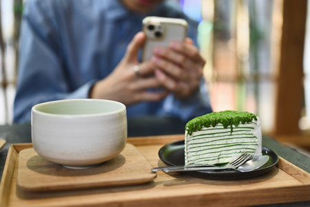 Close up and cropped image of Blogger using smartphone snap a picture of slice of Matcha crepe cake...