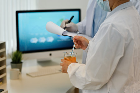 Rear view and close up image of Young Scientist researcher stirs the substance in the beaker while...