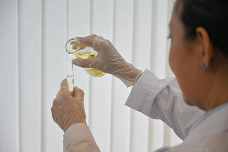 Close up and behind shoulder view image of Middle age Scientist pouring substance from beaker into a...