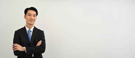Waist up portrait of a Confident Young Asian man in a formal suit standing with arms crossed gesture over a white isolated studio background..の写真素材
