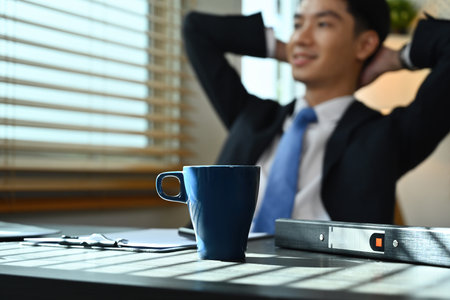 Selective focus on a cup of coffee with businessman relaxing at the working desk on the background.の写真素材