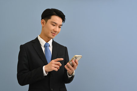 Waist up portrait of Young Asian man in formal suit using mobile phone on color isolated studio background.の写真素材