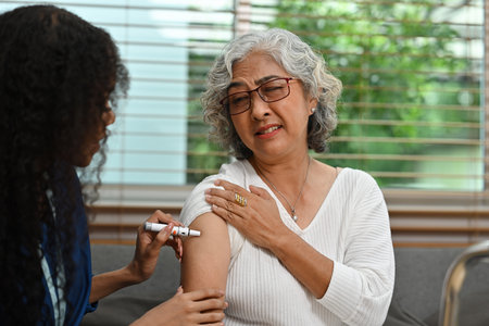 An African nurse or caregiver takes a blood sample of a senior woman's arm with a lancet pen. World Diabetic Day with Senior Diabetic Patient Concept.の写真素材