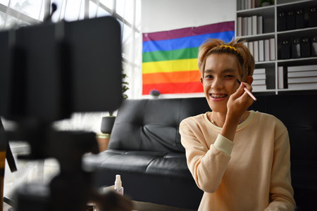 Happy and excited teenage Asian gay streaming a beauty vlog from home, online content creator applying makeup on his face. Cosmetics, Makeup, LGBT people concepts.の写真素材