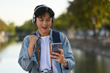Asian tourist with headphones looking on the phone with victory gesture, the Chiang Mai city on the background.の写真素材