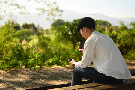 A Lonely Man Using Smartphone When Sitting on the Bench with Outdoors beautiful natural view.の写真素材