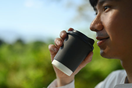Close-up with a Young Asian man drinking a hot drink from a disposable cup.