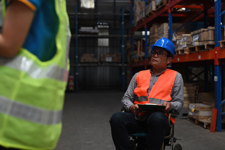 A senior warehouse supervisor with a disability in a wheelchair manages the work with the team, business logistics, and transport concept.の写真素材