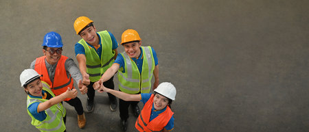 High-angle shot of a group of workers standing and making a thumbs-up gesture to the camera, banner...