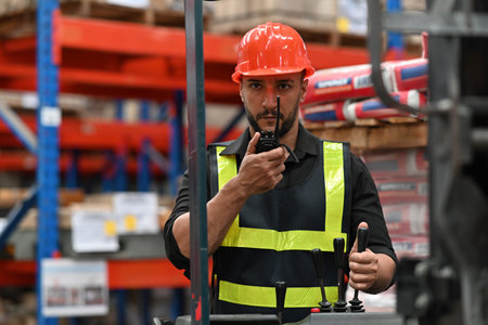 Caucasian man worker driving a forklift and using a walkie-talkie at warehouse factory container, communication radio, Inventory and wholesale concept.の写真素材