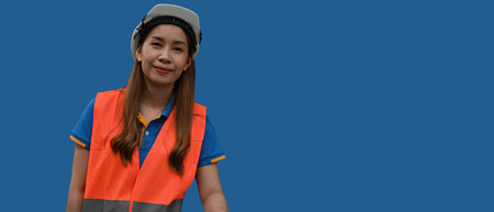 Portrait of Asian Warehouse or Construction worker woman with a hard helmet and reflective safety vest, over blue color background, Banner cover with copy space.の写真素材