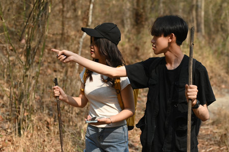 Two young hiking friends are searching for a route together using phone and pointing at their destination with finger.の写真素材