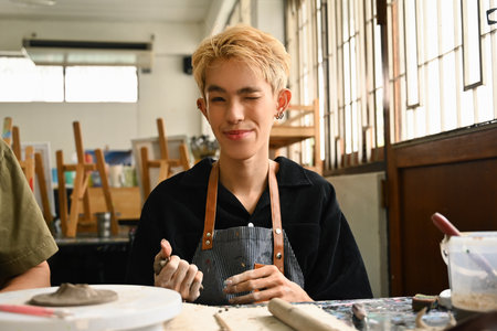 An LGBT artist winks while holding a piece of clay, expressing joy and creativity in a pottery studio. The artist's personality and dedication to their craft in an inspiring workspace.の写真素材