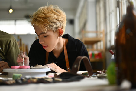 A focused art student meticulously paints a ceramic piece during art class hours, showcasing creativity and concentration in a classroom setting.の写真素材