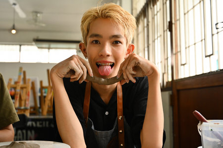 An LGBT artist playfully sticks out their tongue while holding a piece of clay, expressing joy and creativity. The artist's vibrant personality and passion, showcase a lively and inspiring workspace.の写真素材
