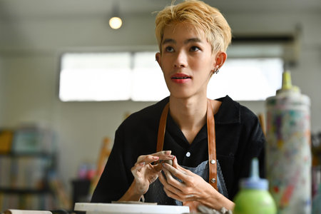 A young LGBT boy with short blonde hair engaged in crafting pottery, The person appears focused and absorbed in their creative process, shaping clay with their hands.の写真素材