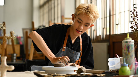 an LGBT person with braces, wearing an apron, pressing clay to form a shape on a pottery wheel. They appear focused and content, working in a bright, art-filled studio.の写真素材