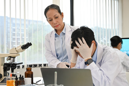 An elderly female scientist consoles a male colleague who is upset over a failed research project or stressed from work.の写真素材