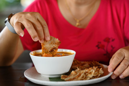 Close-up of woman's hand taking a food bite and eating chapati with Massaman curry.の写真素材