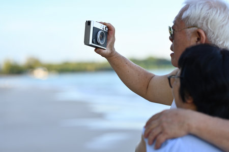 Romantic Senior couple using camera take a picture together on the beach, wedding anniversary and...