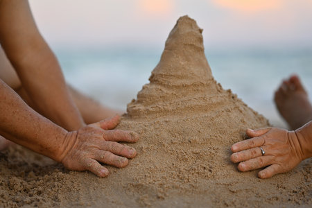 Close-up image of Senior couple's hand playing together in the sand on a tropical beach, Building a sand castle.の写真素材